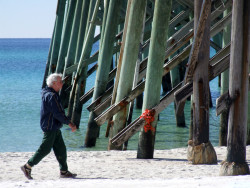 A solitary man walks down the white sands of Panama City Beach, FL, enjoying the florida sun and emerald waters of the Gulf of Mexico.