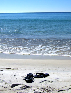 Sandals sitting on the beach as the water from the Gulf of Mexico laps onto shore.