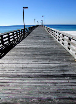 Wooden pier stretches across the white sand of Panama City Beach, FL and out into the Gulf of Mexico.